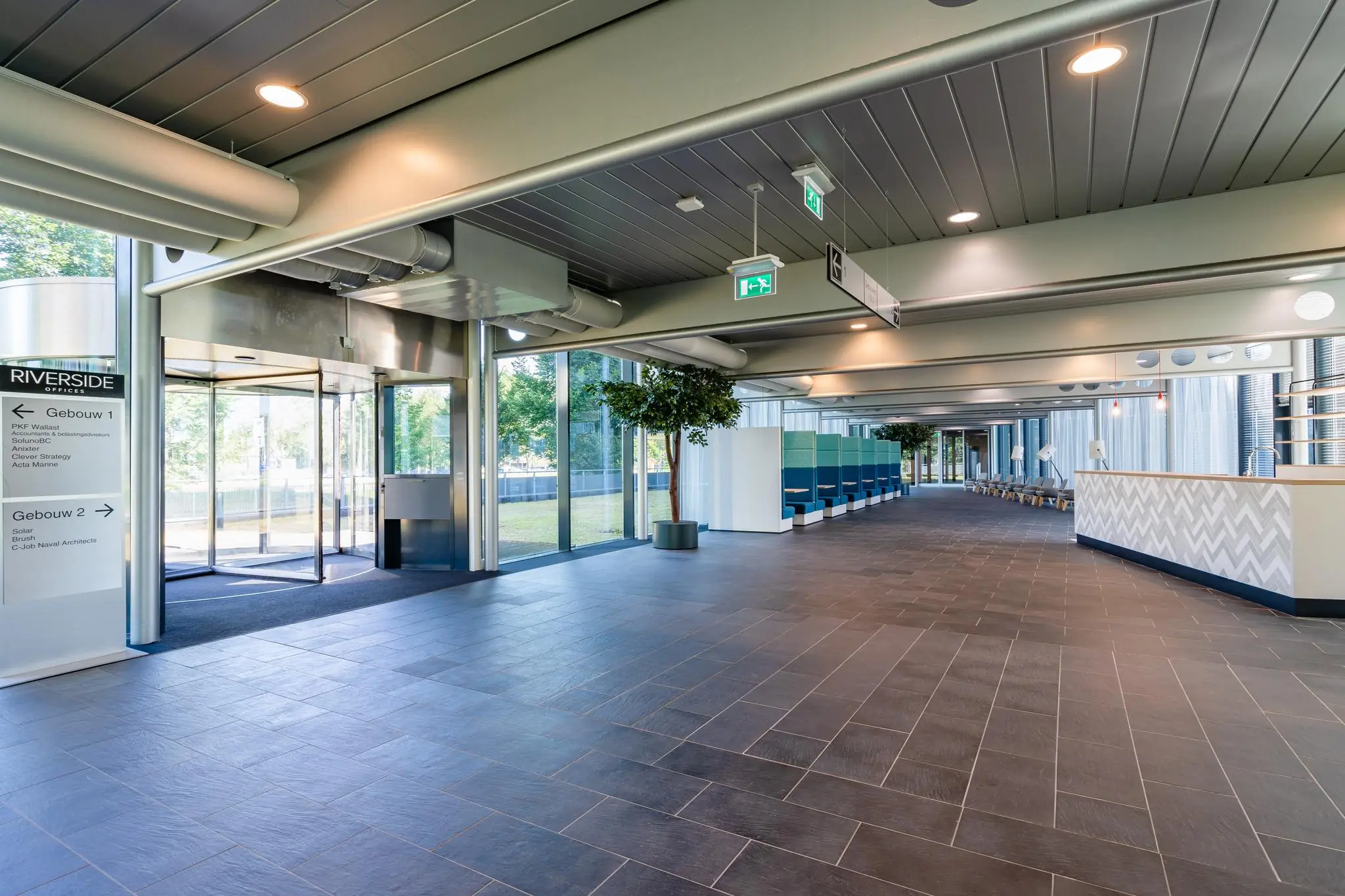 Moderne en lichte entreehal van het Rivium Promenade kantoorgebouw met zitgedeelte en glazen draaideur.